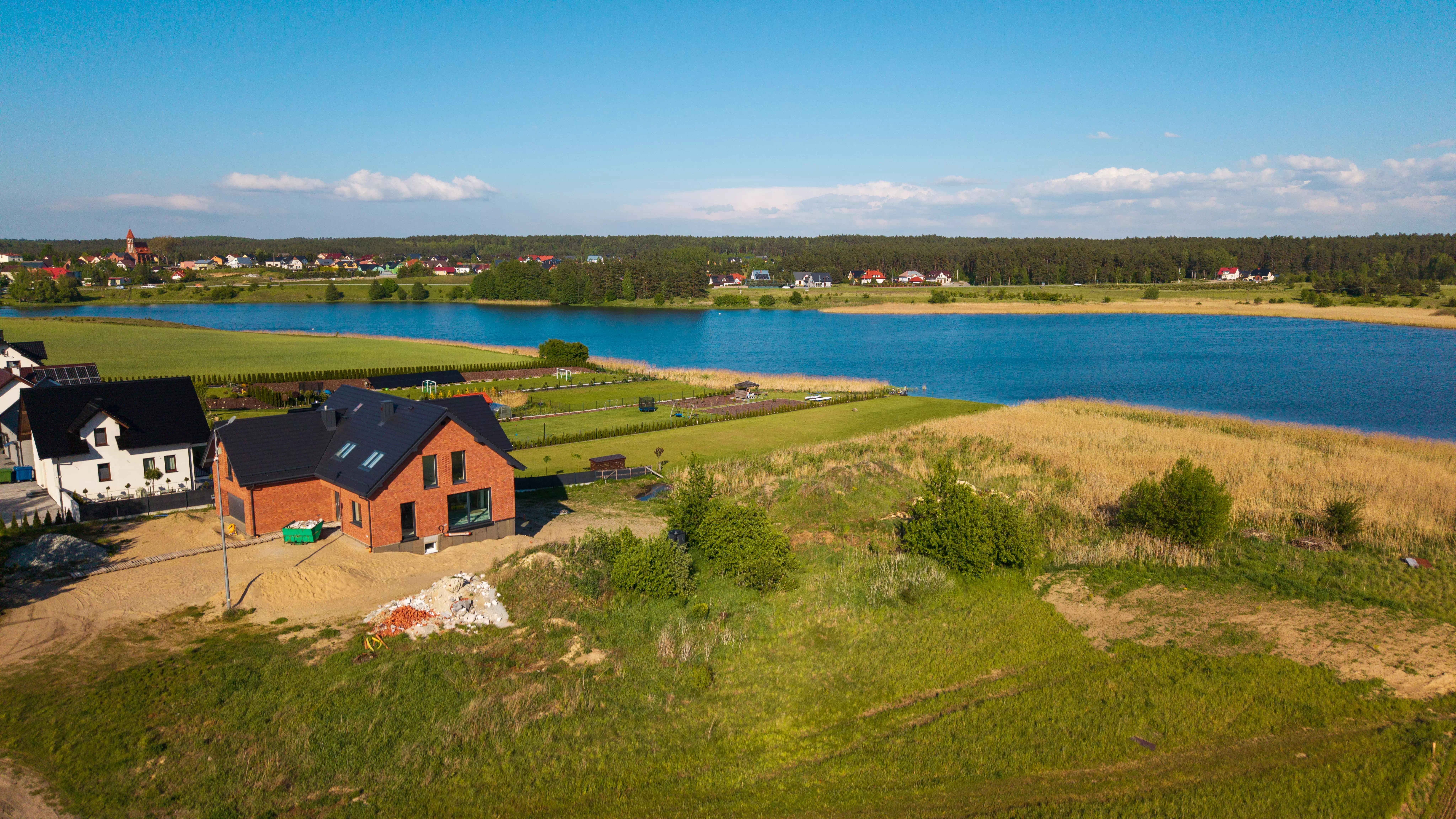 Zabytkowy kościół z czerwonej cegły z wieżą i pomarańczowym dachem, otoczony budynkami i zielenią, widok z powietrza