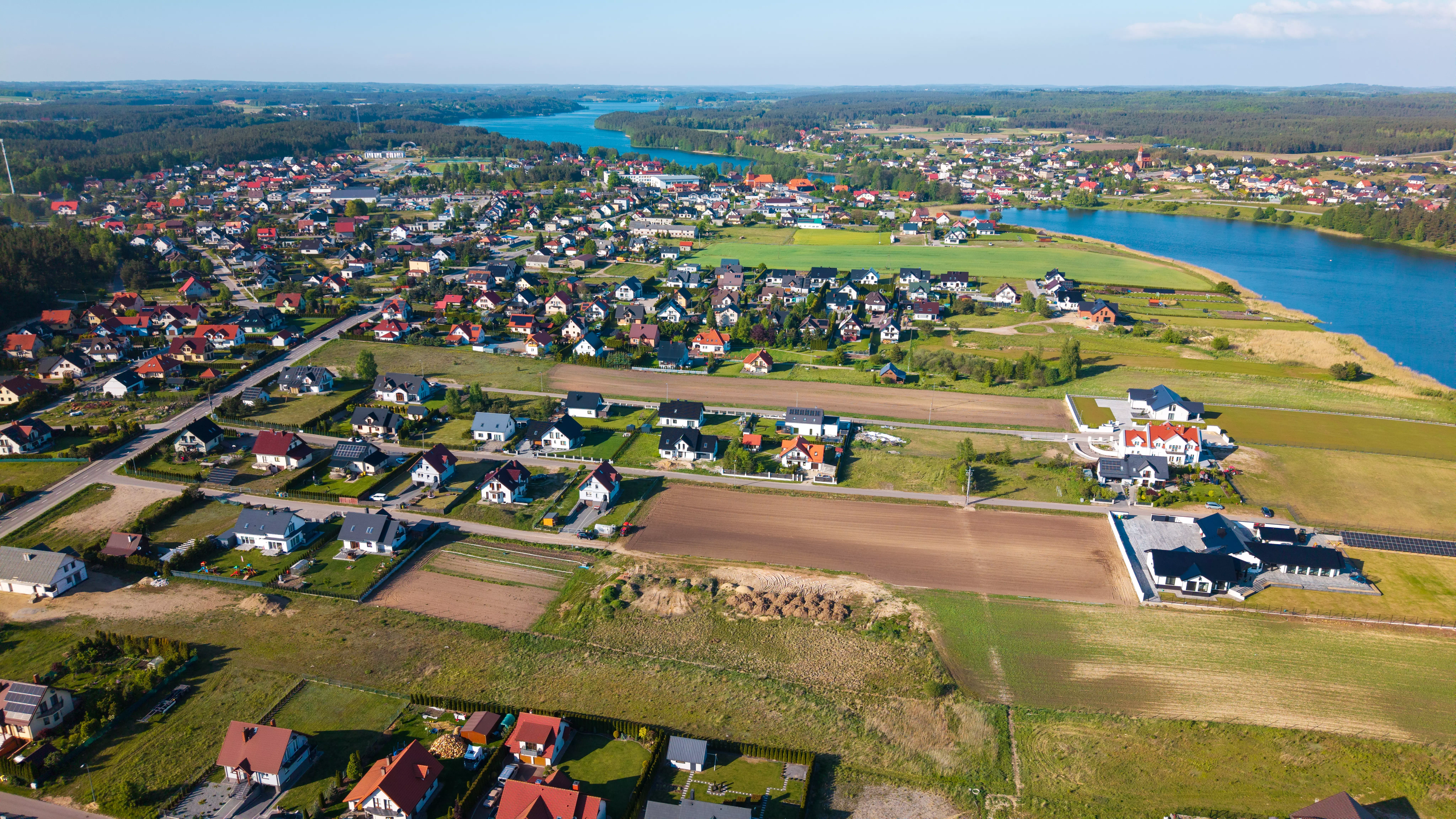 Jezioro otoczone polami, domami i lasami, widok panoramiczny z powietrza przy słonecznej pogodzie