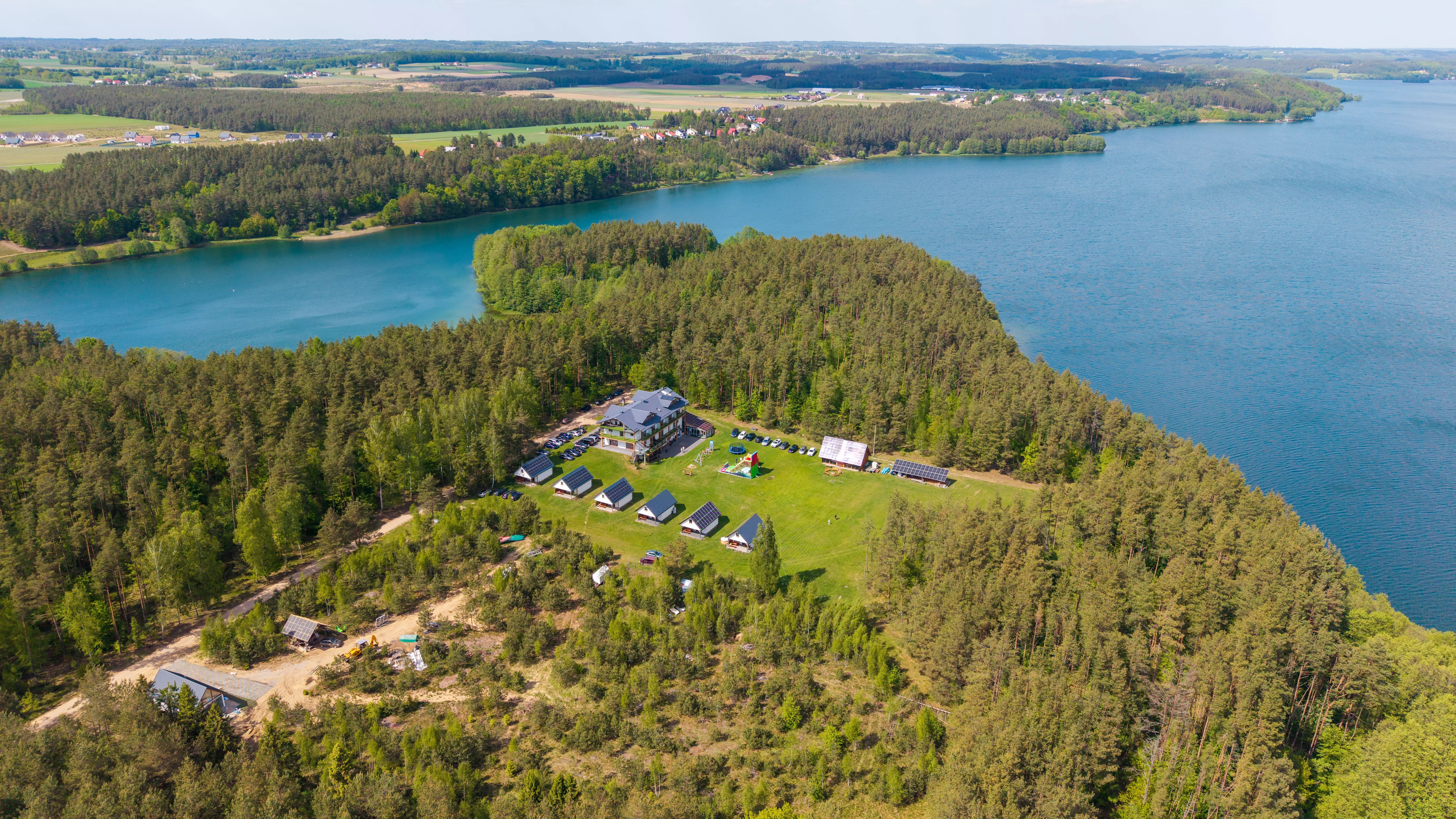 Ośrodek wypoczynkowy z domkami letniskowymi położony wśród lasów nad dużym jeziorem, widok z lotu ptaka