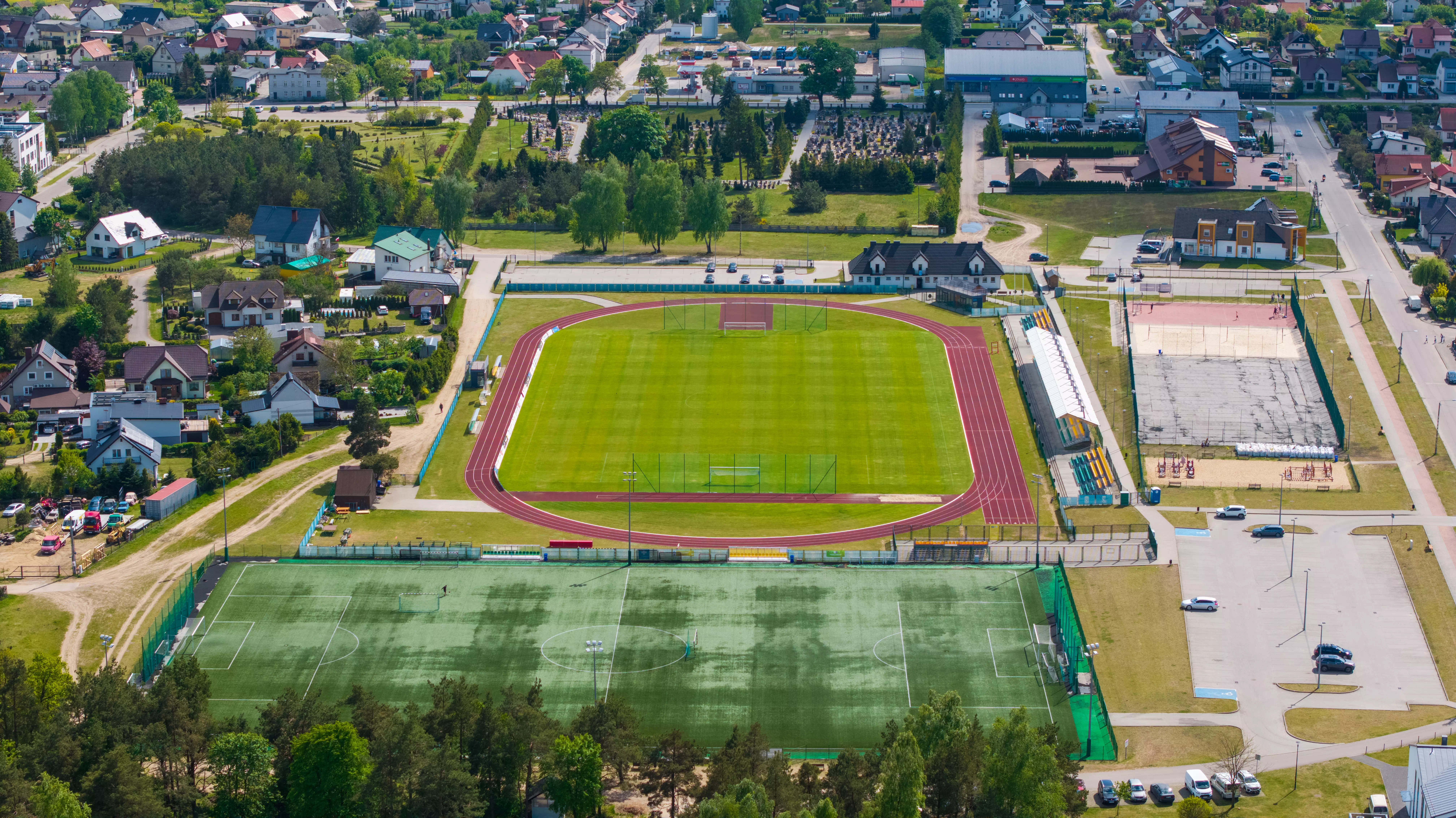 Kompleks sportowy z boiskiem piłkarskim, bieżnią lekkoatletyczną i otaczającymi go zabudowaniami mieszkalnymi, widok z powietrza