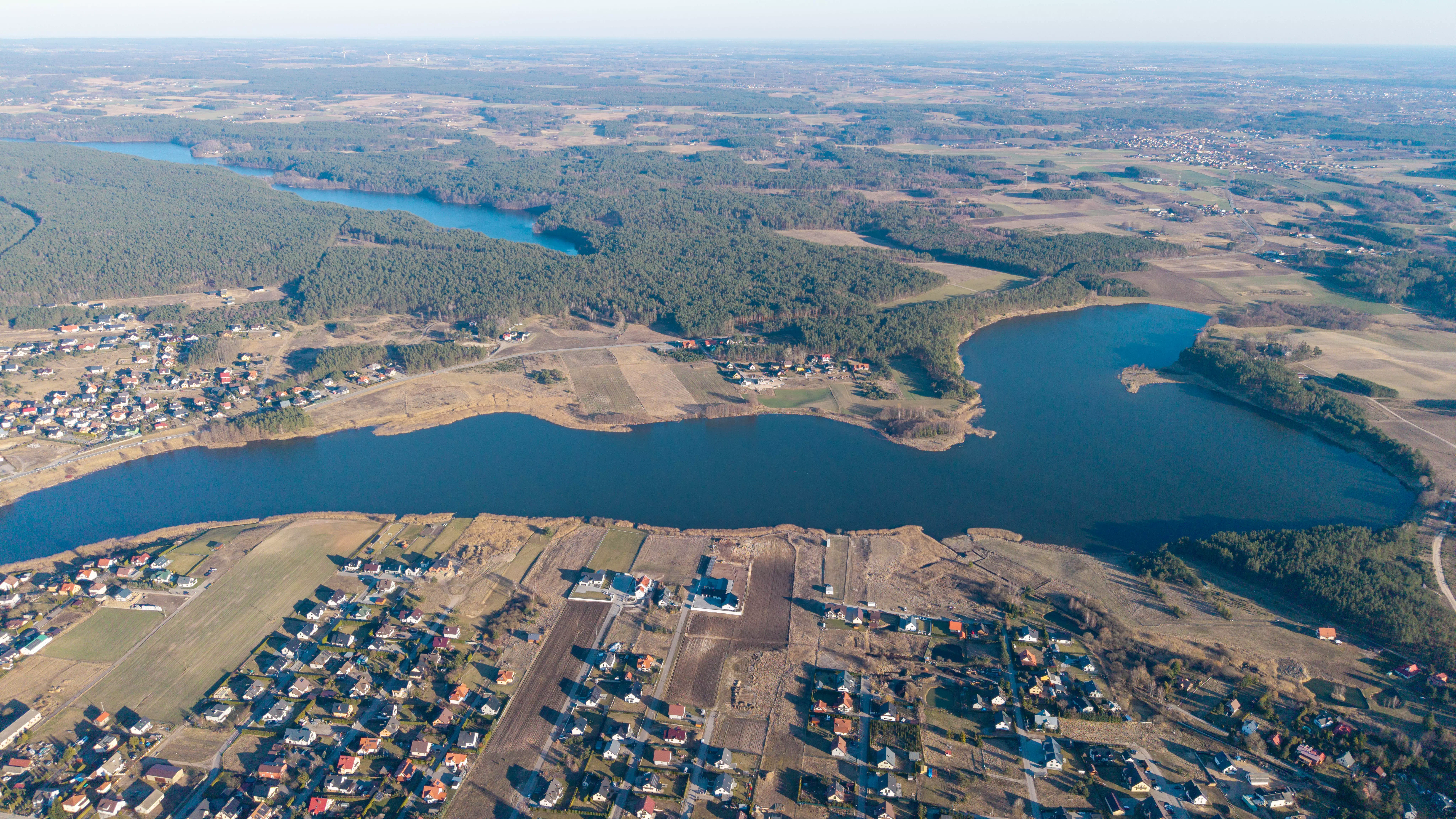Szeroki widok na miasto położone nad jeziorem, otoczone polami i lasami, zdjęcie z powietrza