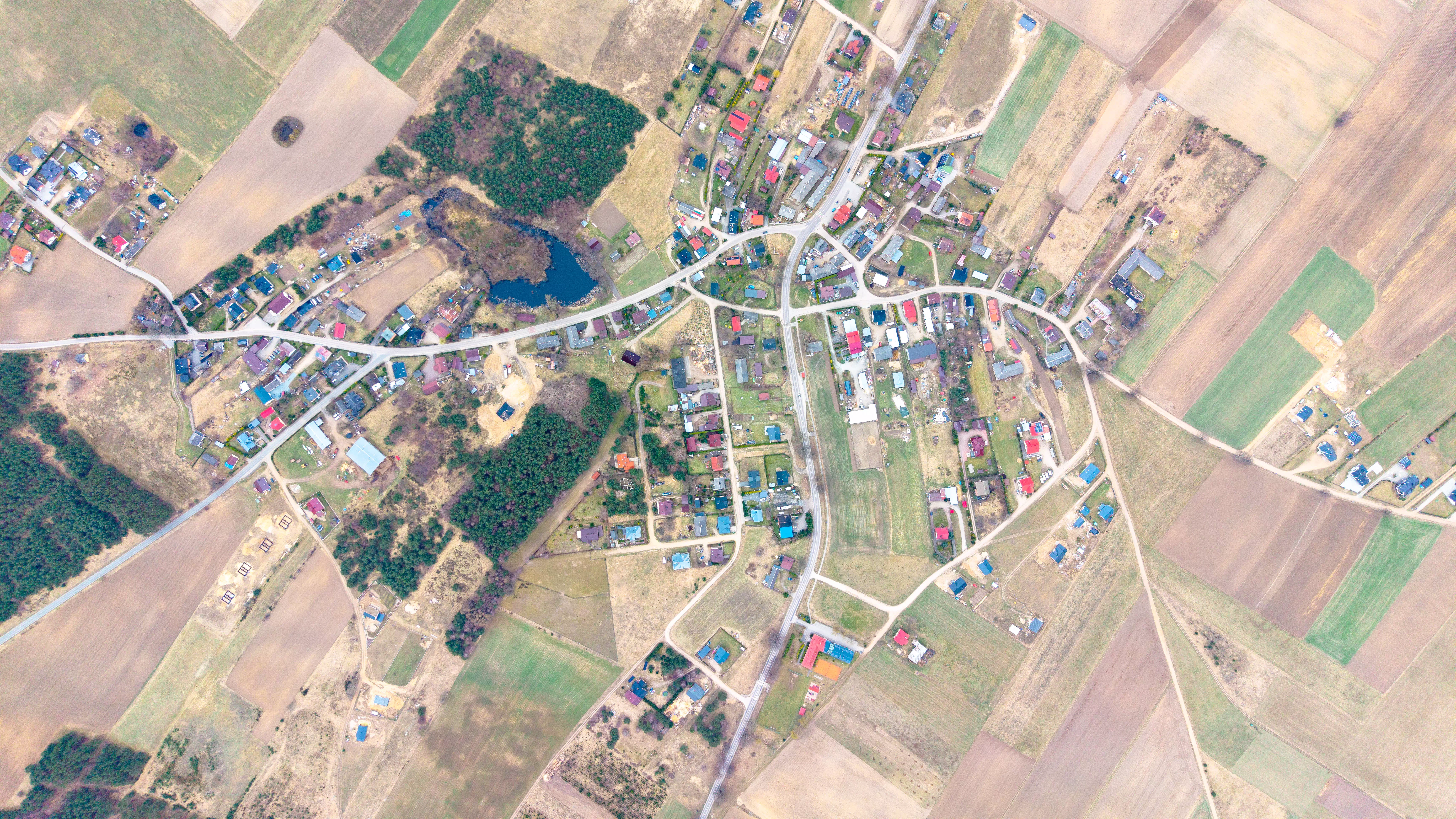 Panorama jeziora wijącego się przez lasy i pola, z fragmentem miasta i stadionem w dolnej części zdjęcia, widok z lotu ptaka