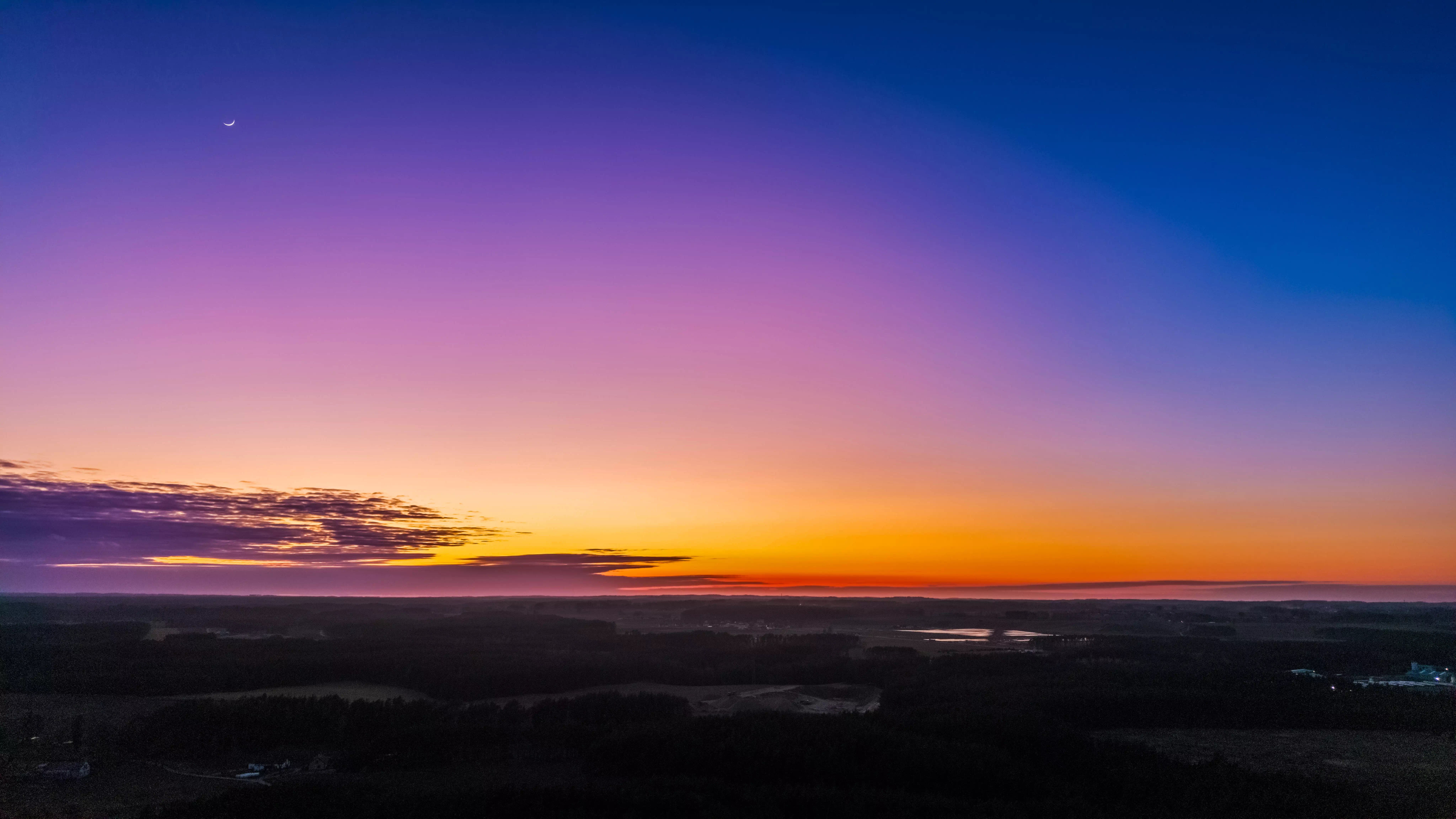 Kolorowy zachód słońca nad rozległym, leśnym krajobrazem z widocznym księżycem na niebie