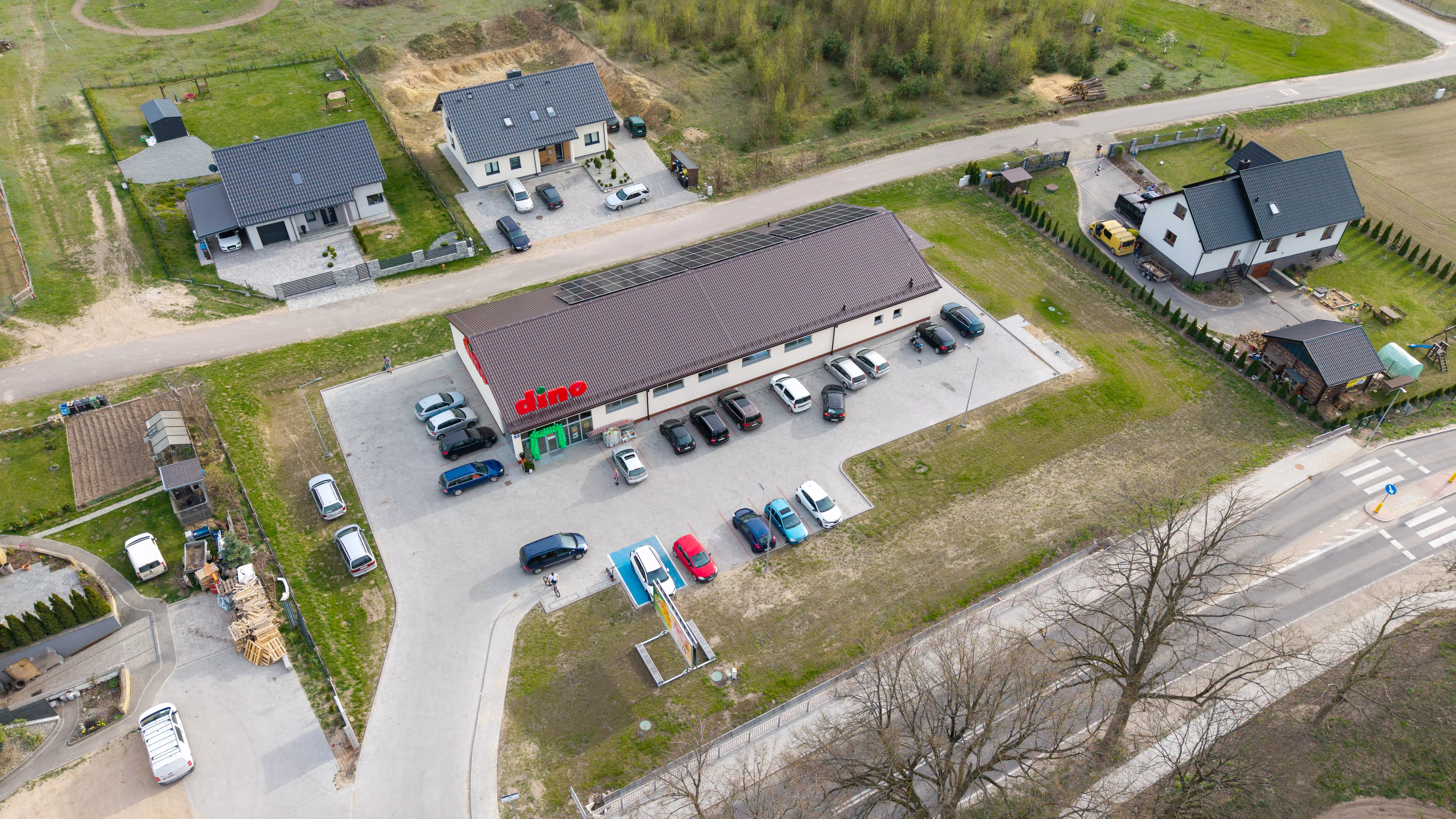 Budynek supermarketu Dino z parkingiem oraz okolicznymi domami, widok z lotu ptaka