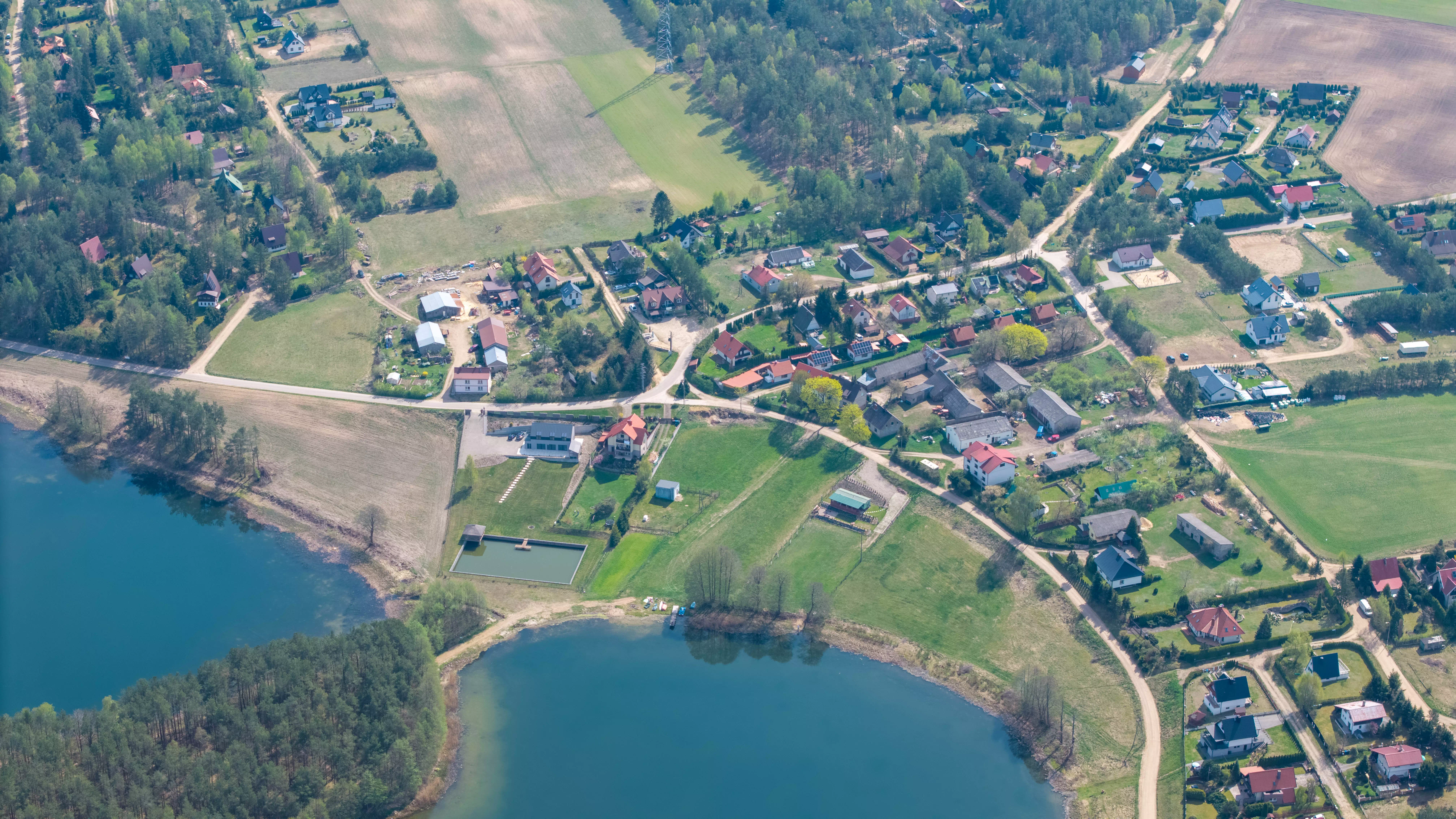 Panorama wsi nad dwoma jeziorami, z zabudową mieszkalną i polami uprawnymi, widok z lotu ptaka